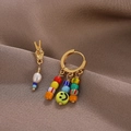 Nahaufnahme asymmetrischer Ohrringe mit Smiley-Perlen und Goldgeste auf braunem Samt - Asymmetrischer Stil / Gold
