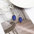 Detail of gold hook earrings with blue oval stone resting on a magazine page - Dark Blue