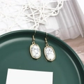 Close-up of golden oval earrings with white marble texture stone on a ceramic plate - White