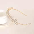 Serre-tête doré avec feuilles en strass brillants posé sur une tasse à café en céramique - Doré