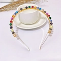 Detalle de diadema dorada fina con cristales de colores sobre una taza de café blanca - Estilo Redondo de Colores (D2513)