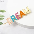 Close-up of golden DREAM letter hair clip with colorful enamel filling on a white stand - DREAM Word Style (C5406)