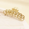 Detailed macro view of a golden metal hair claw clip with interlocking ring design - Gold