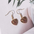 Close-up of heart-shaped gold earrings with colorful glitter inlays on white paper - Purple (E6210)