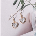 Close-up of golden heart-shaped drop earrings with shimmering silver crystal texture - Light Gray (E6218)