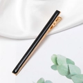 Detail of minimalist black enamel hair clip with golden alloy base on white silk cloth - Black