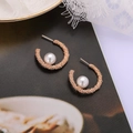 Close-up of rose gold C-shaped pearl earrings with granular texture on vintage book background - C-Shape Rose Gold (A8533)