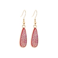 Detailed close-up of golden teardrop earrings with sparkling pink crystal inlay and red trim - Red