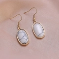 Detail of gold-framed marble drop earrings with white textured stones on pink silk cloth - White