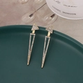 Dettaglio di orecchini geometrici dorati con cristalli scintillanti su ceramica - Oro