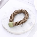 Detail of a brown spiral telephone wire hair tie with a matte green decorative bead - Khaki (K8106)