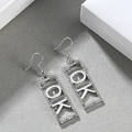Detail silberner rechteckiger Ohrringe mit Strassbesatz und weißem OK-Buchstaben - OK Silber + Weiß