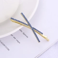 Fermaglio per capelli a croce dorato con strass blu scuro su uno sfondo minimalista - Blu