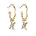 Close-up of golden letter K drop earrings with sparkling crystals on C-shaped hoops - Gold K