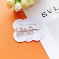 Dettaglio di un fermaglio STAR dorato con strass brillanti su supporto per gioielli - Stile STAR Oro Rosa