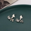 Silberne LOVE Herz-Ohrstecker mit Zirkonia auf einem grünen Dekoteller präsentiert - Silber
