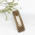 Dettaglio di un fermaglio BB dorato rettangolare con perle marroni su lino bianco - Quadrato Marrone Champagne (C2333)