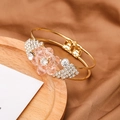 Detail of gold floral open bangle with pink crystal petals on a brown silk background - Pink