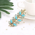 Close-up of golden leaf hair clip with sky blue crystals on elegant white mesh background - Light Blue (H6306)