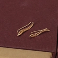 Golden leaf-shaped ear cuff earrings with detailed grain patterns on red background - Gold
