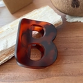 Détail de la pince à cheveux lettre B en motif écaille sur fond en bois naturel - Tortue Mate - Lettre B (Env. 7cm)