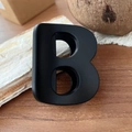 Pince à cheveux noire mate en forme de B posée sur une surface en bois naturelle - Rouge Ancora - Lettre B (Env. 7cm) Noir Mat