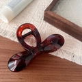 Detail view of a 10.5cm amber resin bow hair claw clip on a warm wooden background - Glossy Tortoise Shell Bowknot