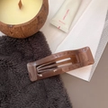 Detail shot of a rectangular amber hair claw clip in a warm minimalist lifestyle setting - Transparent Brown