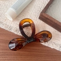 Detail view of amber resin bow hair claw clip with golden metal spring on white fabric - Glossy French Bowknot