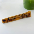Detail einer kreativen Schildpatt-Haarspange in Tubenform mit goldenem Text auf weißem Grund - Brauner Sonnencreme-Entenschnabelclip
