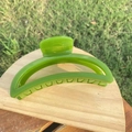 Close-up of bright green crescent hair claw clip on wooden stand with outdoor grass background - 12cm / Turquoise Green Crescent
