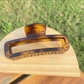 Close-up of tortoise shell pattern hair claw clip on wooden display in nature setting - approx 11.8cm / Extra Large Matte Light Tortoiseshell Bottle