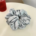 Gros plan sur grand chouchou en satin argenté avec texture plissée sur table - Gris Argent
