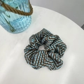Dettaglio dell'elastico per capelli con motivo a zigzag blu e marrone su tavolo bianco - Elastico per Capelli Francese con Motivo a Greca