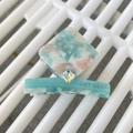 Detail einer blauen Acetat-Haarklammer mit Marmormuster, Kristall und Logo - Ca. 6cm / Blau