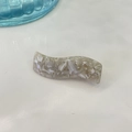 Close-up of wavy acetate hair clip with ivory marble texture and golden handmade logo - Grey White Texture