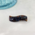 Macro detail of wave-shaped tortoiseshell acetate hair clip with gold logo text - Blue Tortoise