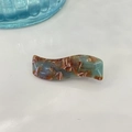 Macro shot of S-shaped marble acetate hair clip with gold logo detail on white background - Marble