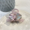 Macro detail of acetate bow hair claw with colorful marble texture and golden lettering - Water Pink Purple