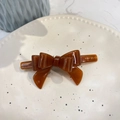 Close-up of caramel brown acetate bow hair clip with gold lettering on a ceramic plate - Crooked 3D Bow (Approx 9cm) / Chocolate Jelly