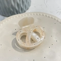 Detalle de una pinza para el cabello de acetato crema con cuentas plateadas en plato de cerámica - Amarillo