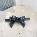 Close-up of a dark grey acetate hair clip featuring a layered 3D bow design and gold logo - Crooked 3D Bow (Approx 9cm) / Jelly Grey