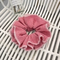 Klassischer rot-weißer Karo-Scrunchie mit Falten auf weißem Zaunhintergrund - Rotes Karo Scrunchie