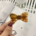 Detailed close-up of a resin bow hair clip with colorful woven edges and a black star detail - Brown