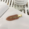 Detailaufnahme einer glitzernden braunen Haarspange mit goldener Metallklammer - Orange