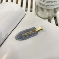 Detailansicht einer grauen Glitzer-Haarspange mit goldener Metallbasis auf einem Buch - Grau