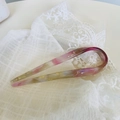 Detailansicht der U-förmigen Acetat-Haargabel mit pastellener Marmortextur auf weißer Spitze - Rosa Meerjungfrau-Stil