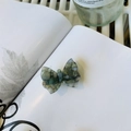 Dettaglio del fermaglio per capelli a farfalla in acetato con texture verde su libro - Blu Speciale