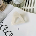 Detail of a creamy beige triangular hair claw clip showing smooth finish and hollow design - Jelly White