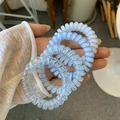Close-up of four spiral telephone cord hair ties in assorted colors held by hand - Blue Ocean Style